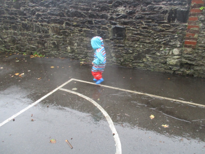 Child in blue and red puddle suit splashes in a puddle.