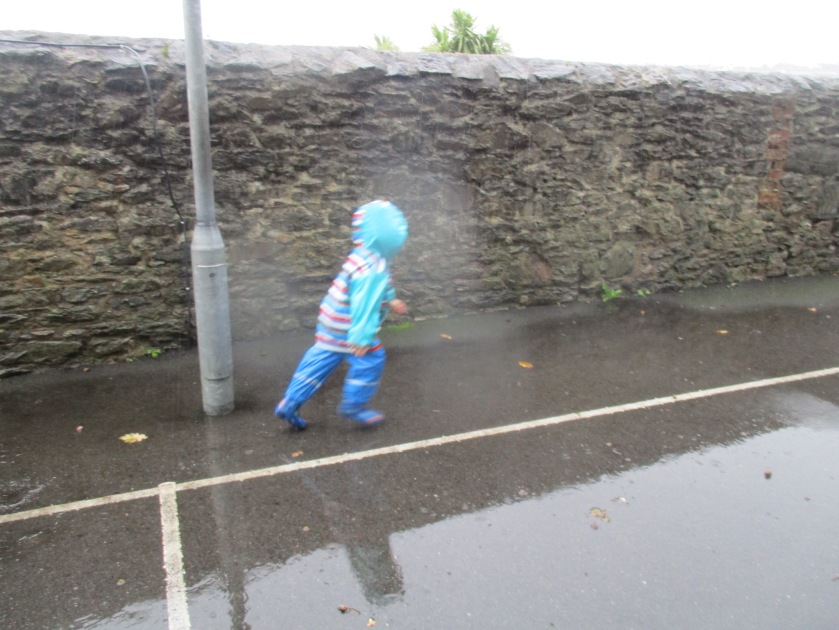 Child in blue puddle suit runs in the rain.